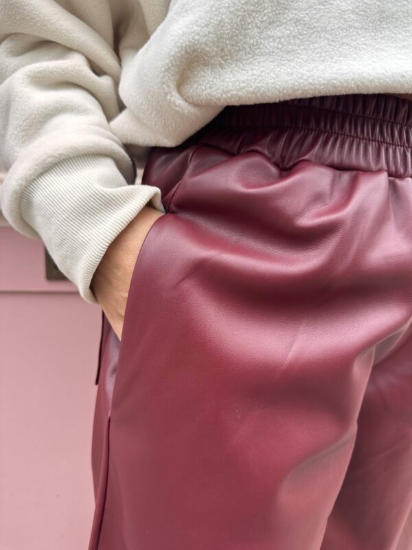 Short MILO bordeaux avec un eslastique au niveau de la taille. Un short aspect vintage mais très moderne, un visuel en similicuir. Porté avec un pull a fermeture éclaire et des basket blanche. La photo est prise sur un mur rose. ( photo zoomé sur la poche)