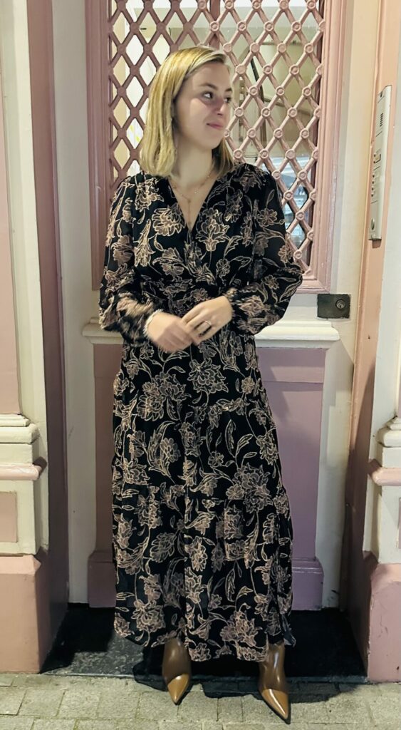 Robe REBECCA, une robe noir longues fluide avec détails fleuries marrons avec les contours dorée. Robe avec des manches légèrement transparentes, une encolure V avec une pression pour une possibilité d'agrandir le décolleté. Cette robe est portée avec les bottines LOUISE, bottines couleur camel à bout pointu.